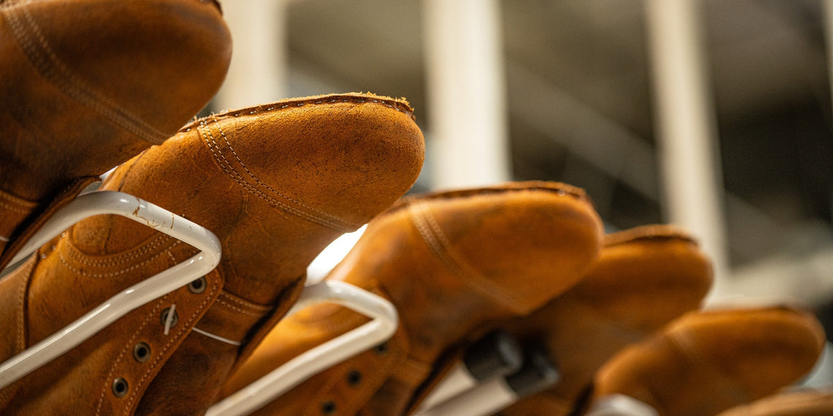 view from below of production rack filled with textured orange coach rambler leather boots in process