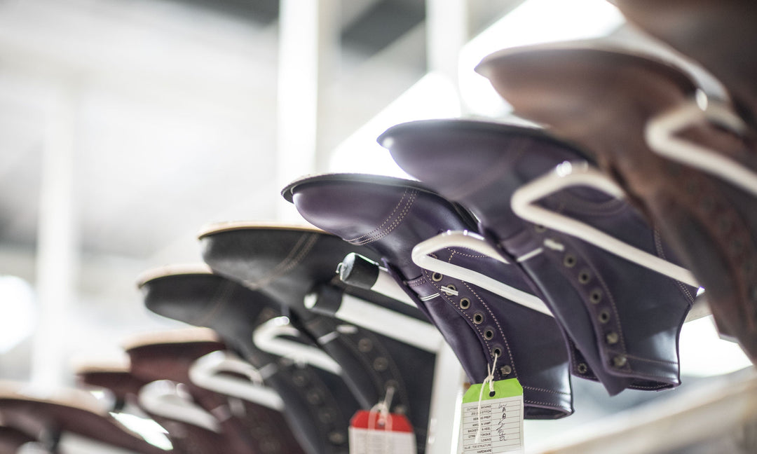 a pair of purple horse rump leather boots upside down on white production rack