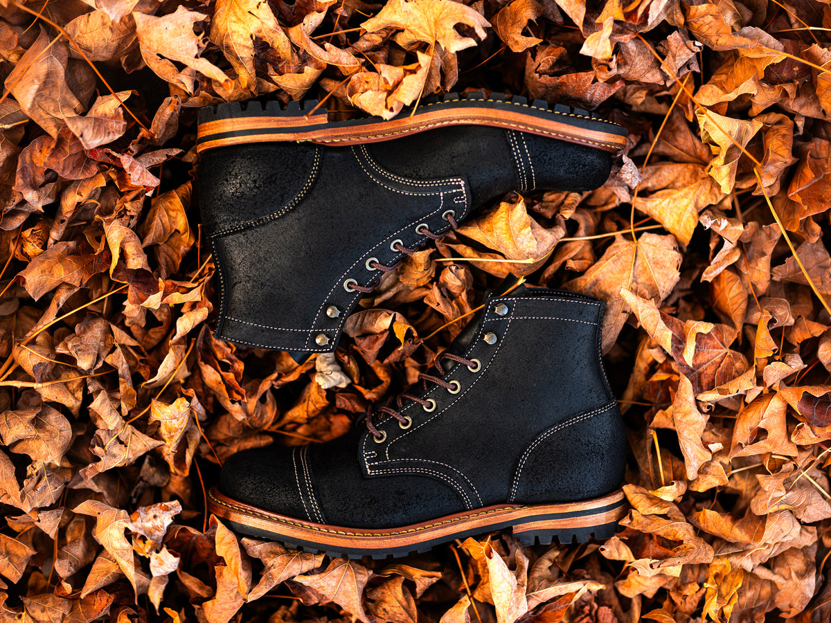 pair of black oiled rough out boots laying on fallen leaves