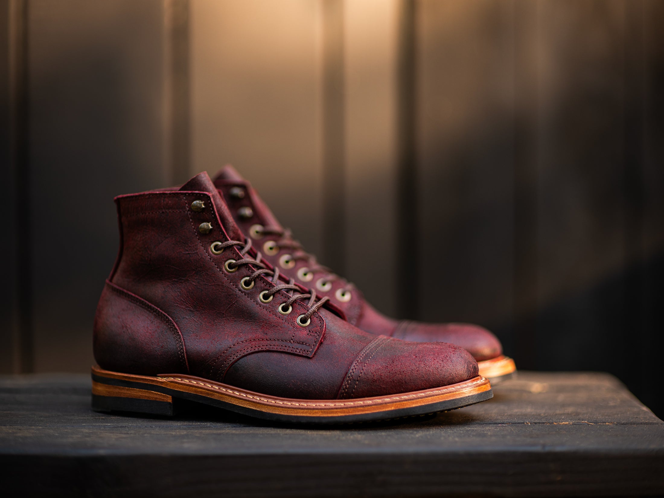 pair of burgundy rambler boots on black wood table with warm light in background