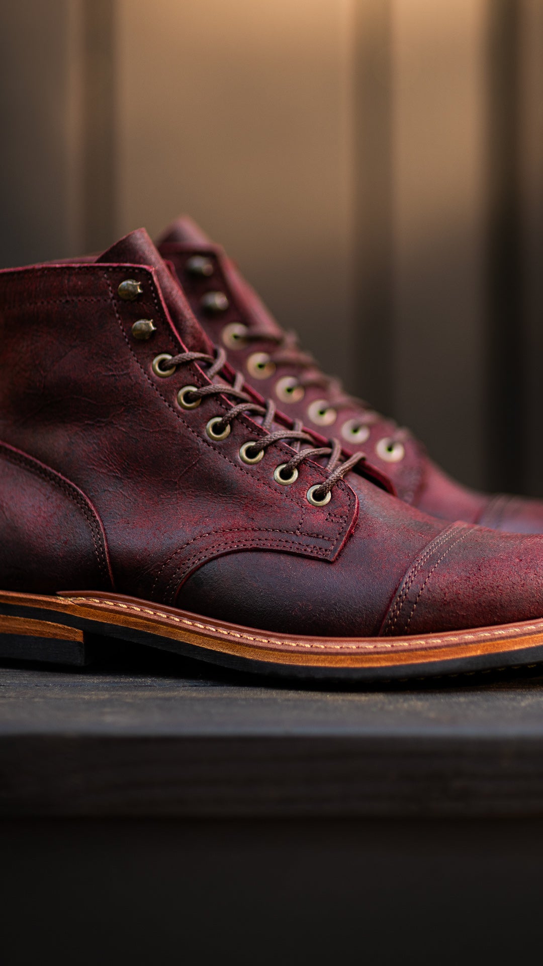 pair of burgundy rambler boots on black wood table with warm light in background