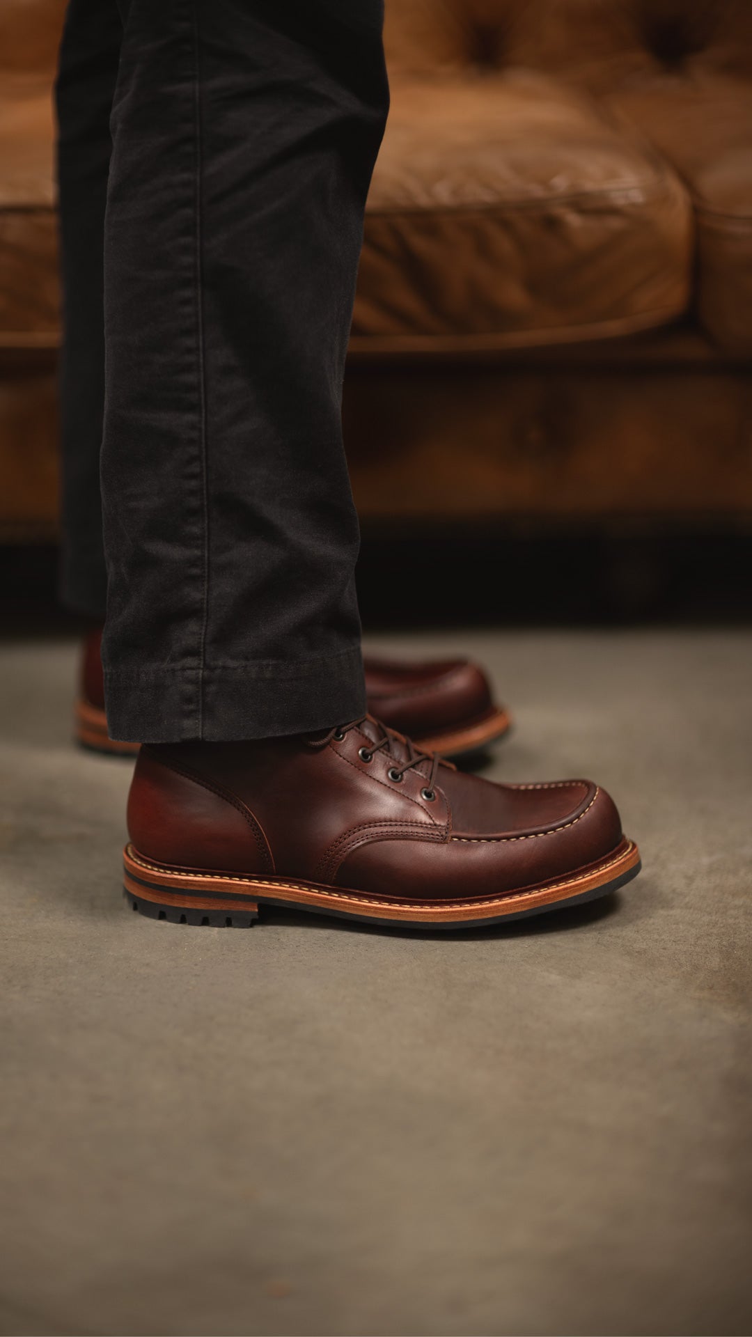 side view of rich brown moc toe boots standing near leather couch