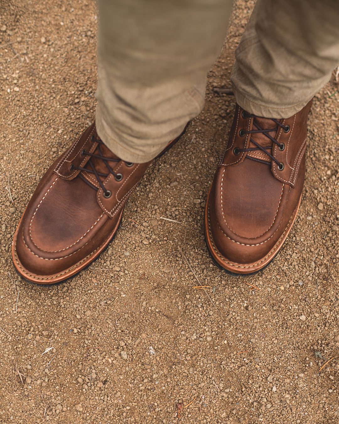 topdown view of man in khaki pants and brown leather moc toe boots on gravel background