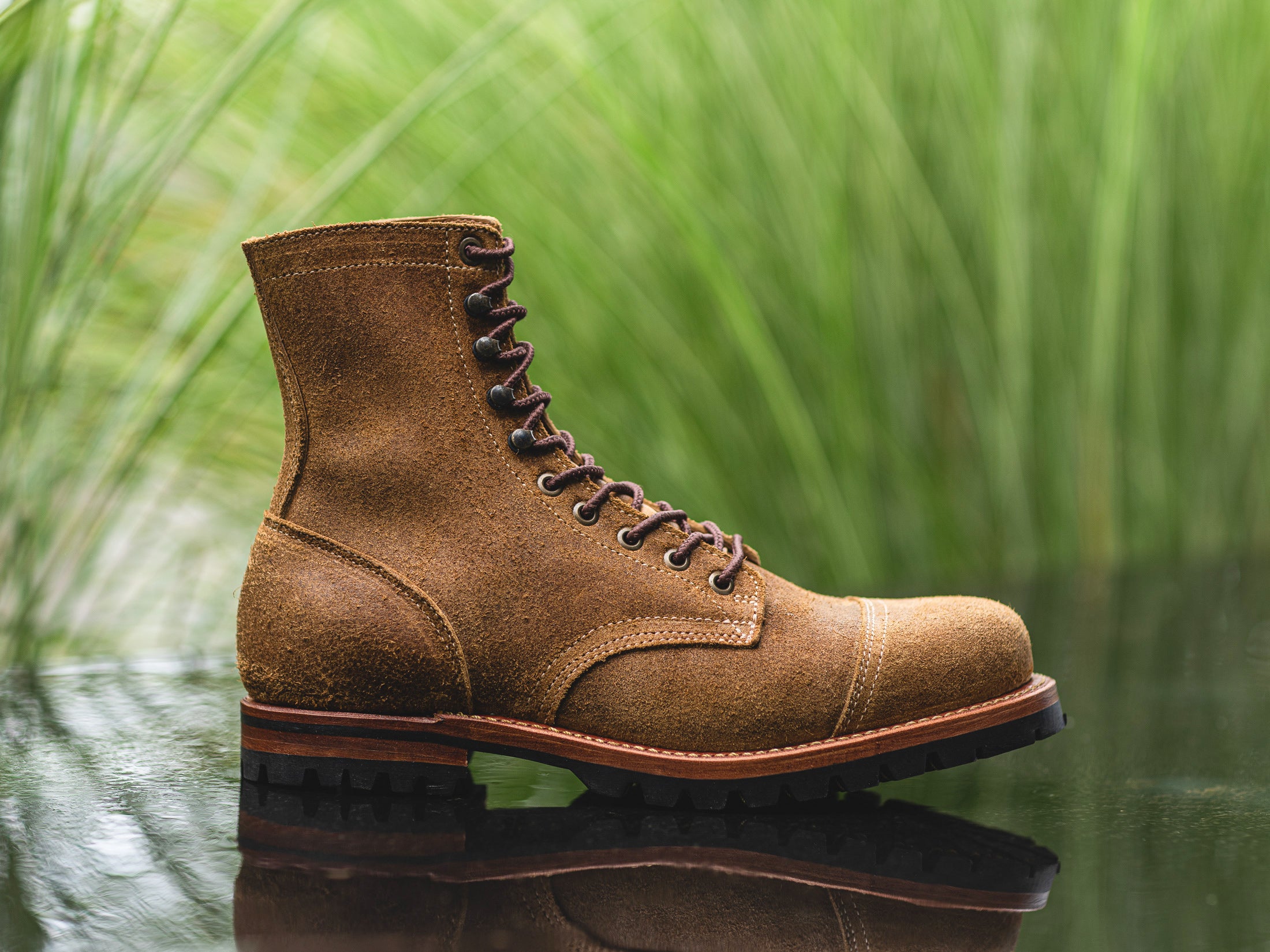 side view of coyote oiled rough out upland boot with shallow depth of focus against out of focus greenery