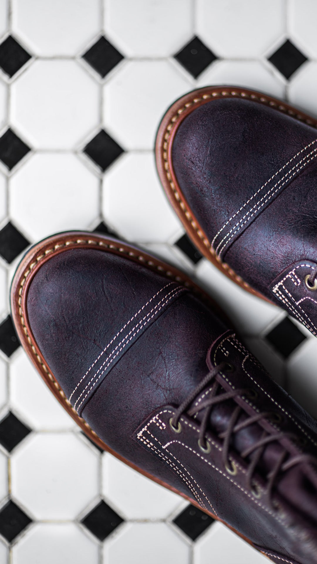 topdown view of pair of garnet rambler cap toe boots on black and white tile