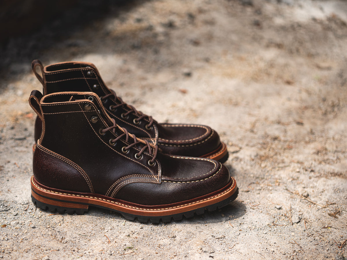 pair of brown waxed flesh leather moc toe boots on gravel close up