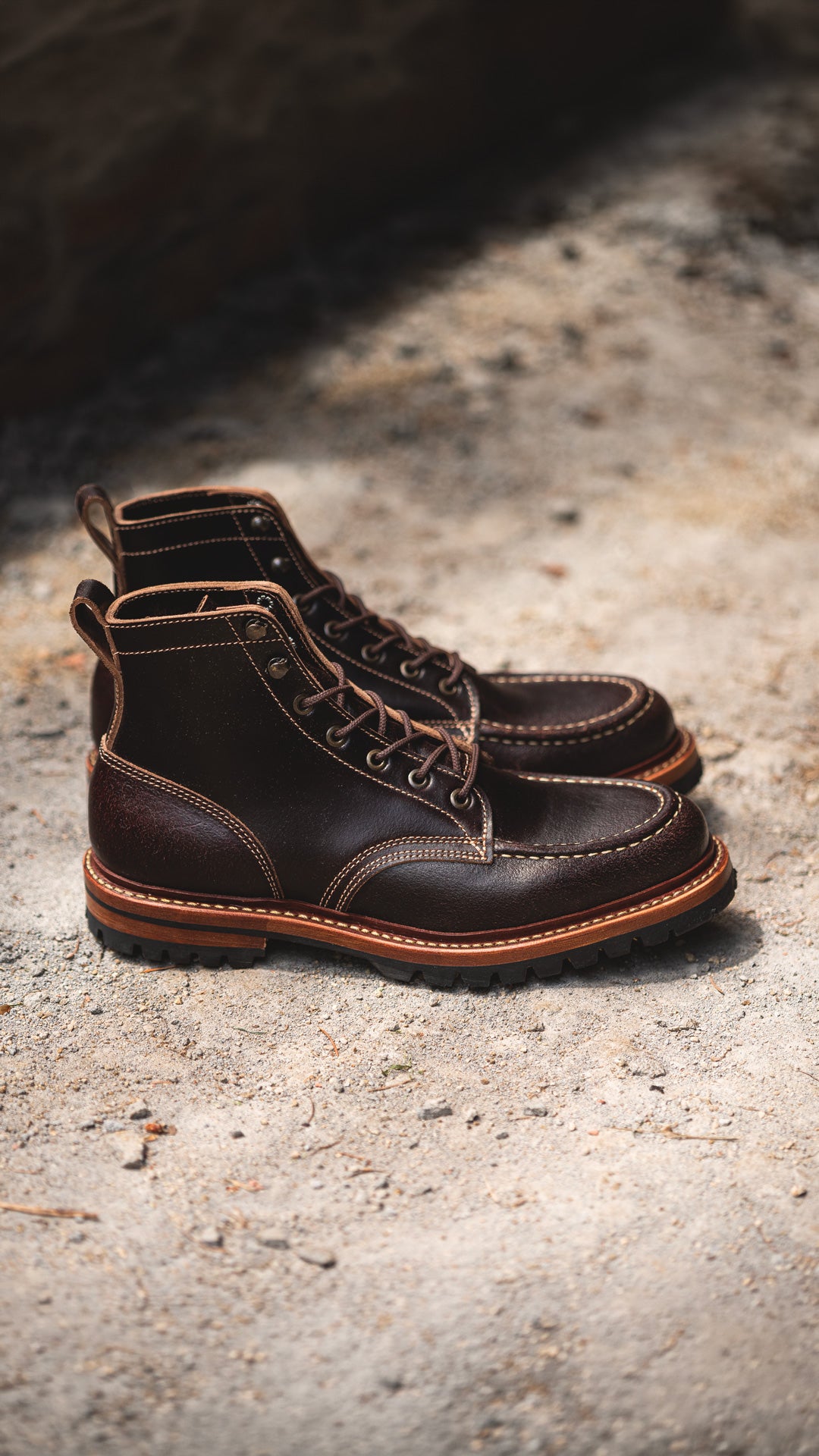 pair of brown waxed flesh leather moc toe boots on gravel close up