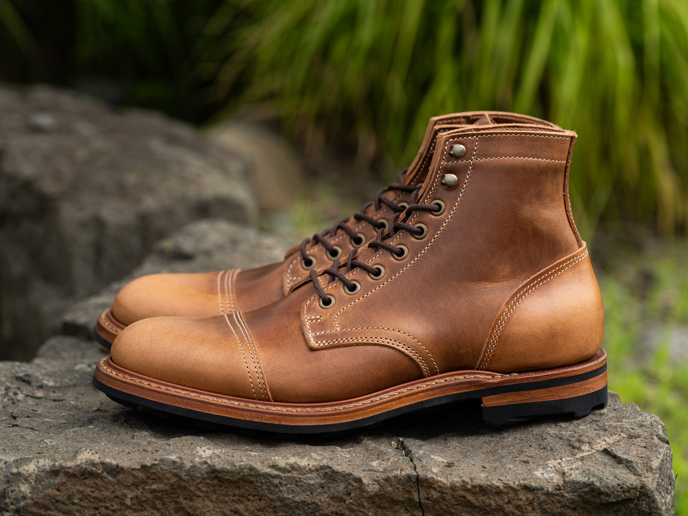 pair of caramel tan boots sitting on stone with green in background