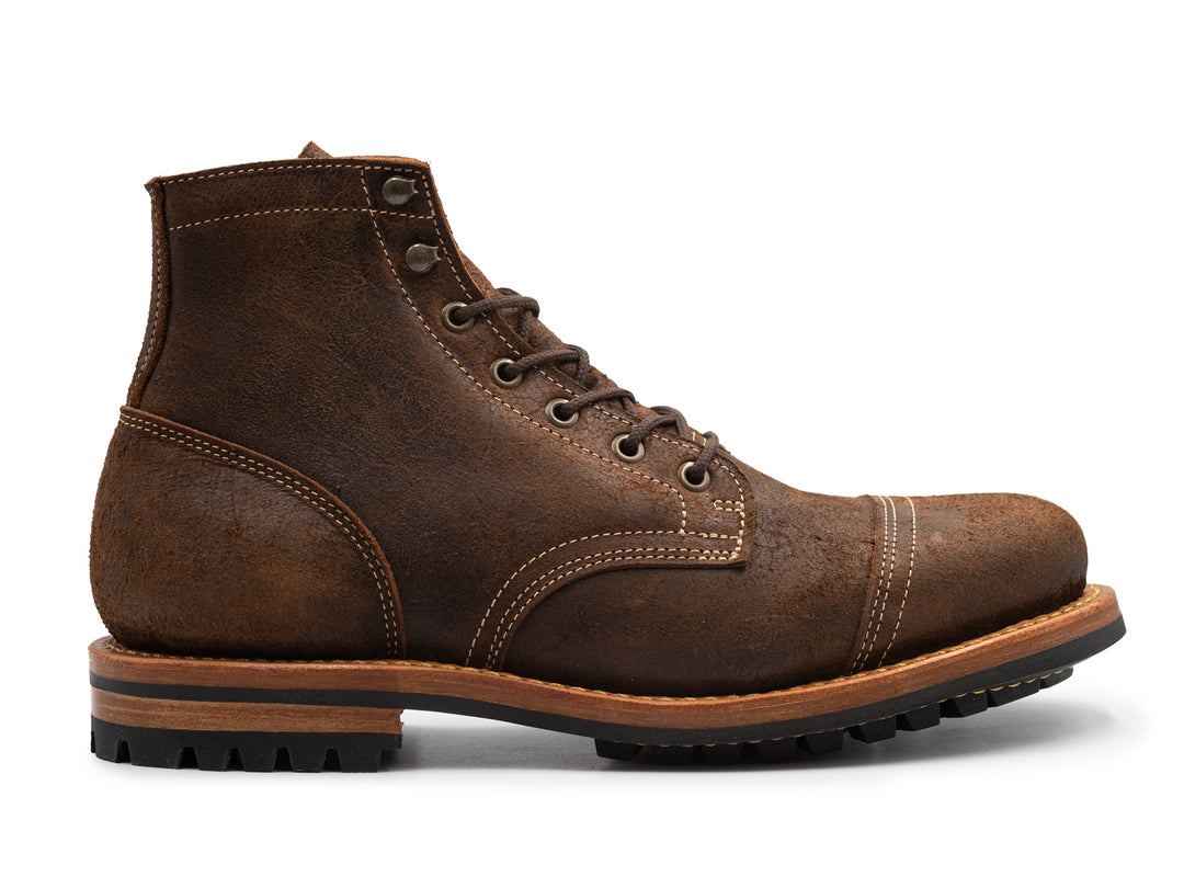 side view of brown textured leather boot on white background