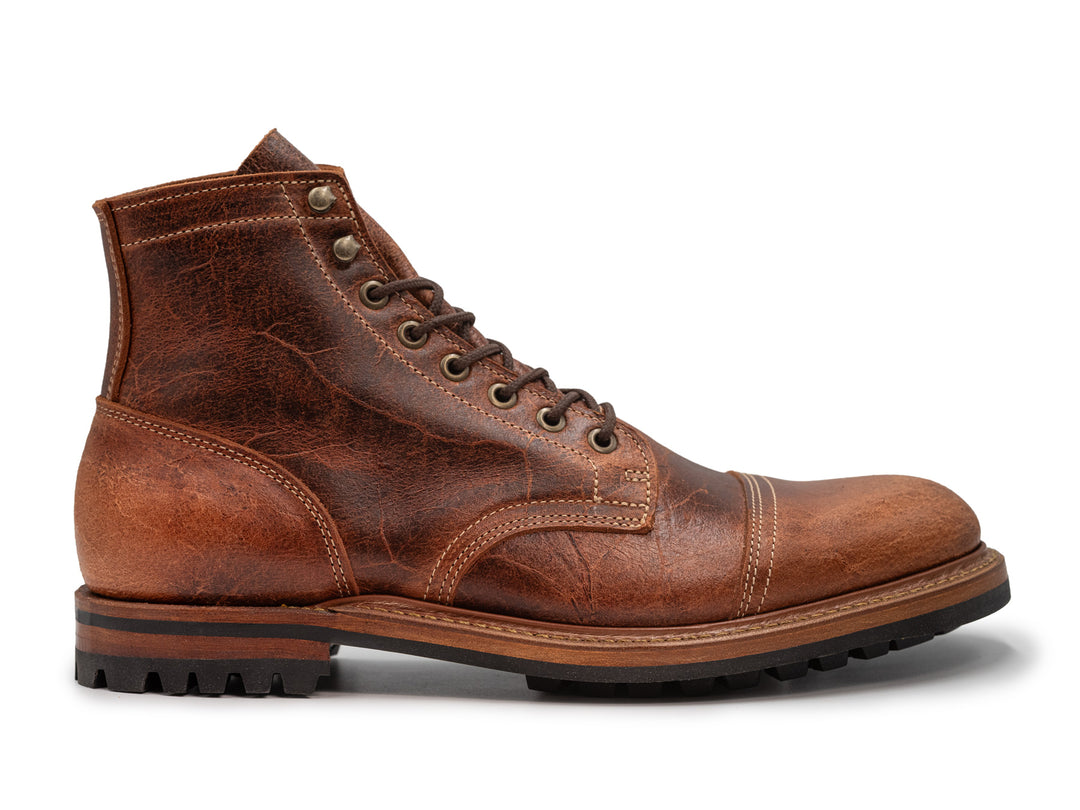 side view of reddish brown textured leather boot on white background